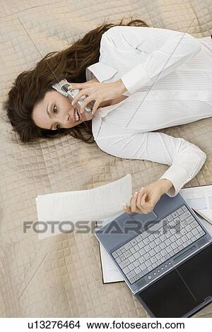 Businesswoman on mobile phone while lying on bed View Large Photo Image Picture - Businesswoman on mobile phone while lying on bed. Fotosearch