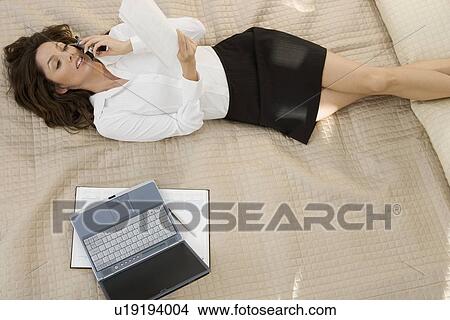 Picture - Businesswoman on mobile phone while lying on bed. Fotosearch