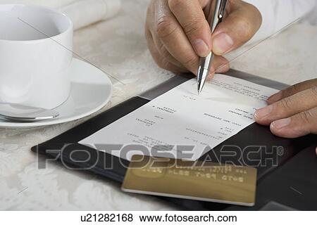 Stock Photo - Close up of man signing credit card receipt at restaurant. Fotosearch