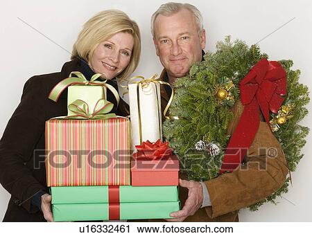 Stock Image - Couple holding Christmas gifts and wreath. Fotosearch
