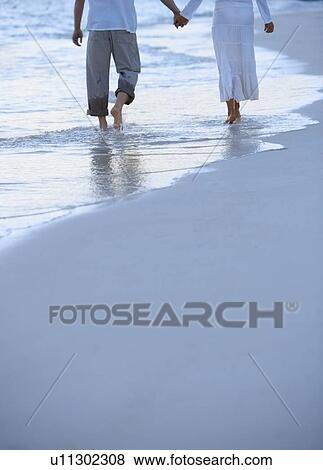 Couple walking along a beach View Large Photo Image Stock Photo - Couple walking along a beach. Fotosearch