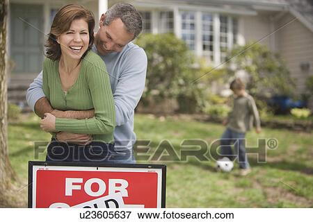 Stock Photo - Family in front of house with For Sale/Sold sign. Fotosearch