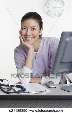 Stock Image - Female healthcare worker leaning on desk. Fotosearch