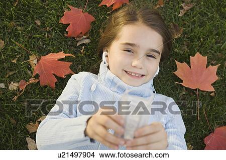 Picture - Girl lying on grass listening to music. Fotosearch
