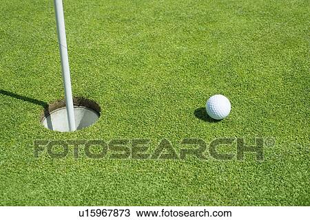 Stock Image - Golf ball near cup on putting green outdoors. Fotosearch
