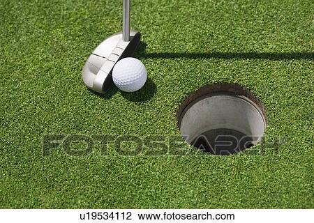 Stock Image - Golf ball near cup on putting green outdoors. Fotosearch