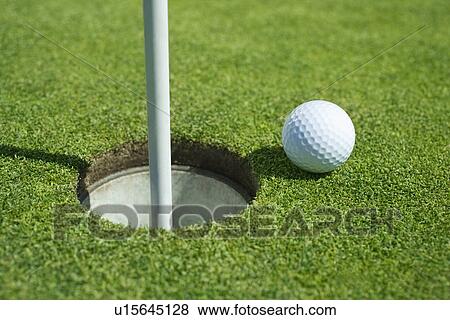 Stock Photo - Golf ball near cup on putting green outdoors. Fotosearch