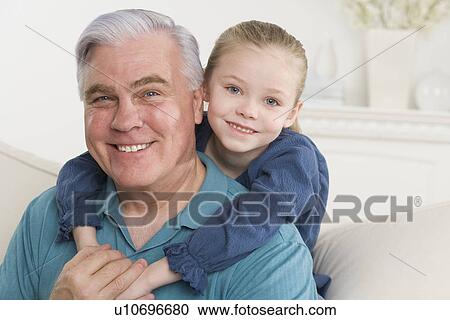 Stock Image - Grandfather and young granddaughter hugging on sofa. Fotosearch