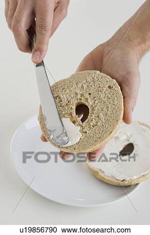 Stock Image - Hand spreading cream cheese on bagel. Fotosearch