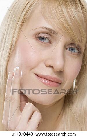 Stock Image - Headshot of woman applying face cream. Fotosearch