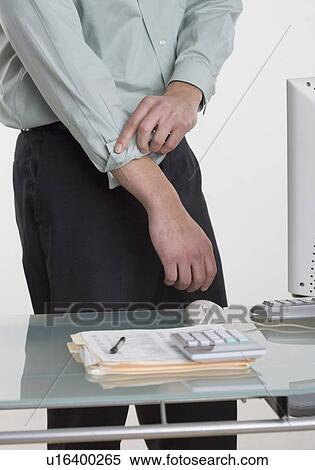 Stock Photography - Man at desk rolling up his shirt sleeves. Fotosearch