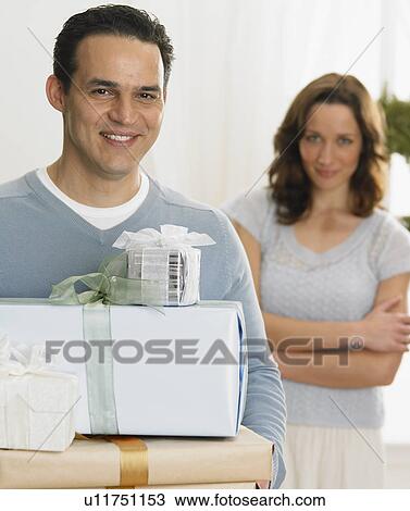 Man holding Christmas gifts with woman in background View Large Photo Image Stock Image - Man holding Christmas gifts with woman in background. Fotosearch