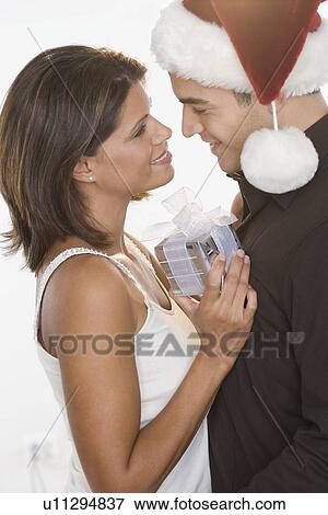 Stock Photo - Man in Santa hat giving gift to woman. Fotosearch