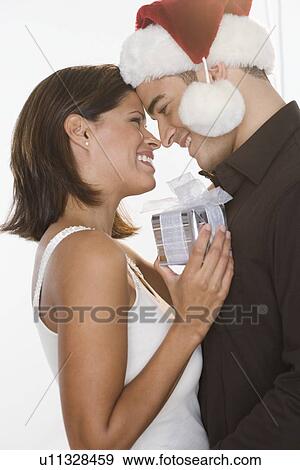 Stock Photo - Man in Santa hat giving gift to woman. Fotosearch
