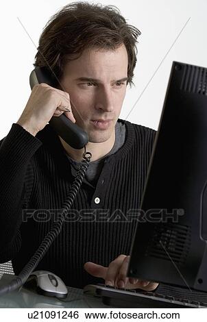 Stock Photograph - Man on phone at computer. Fotosearch