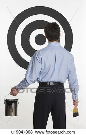 Stock Photo - Man painting bull’s eye on wall. Fotosearch