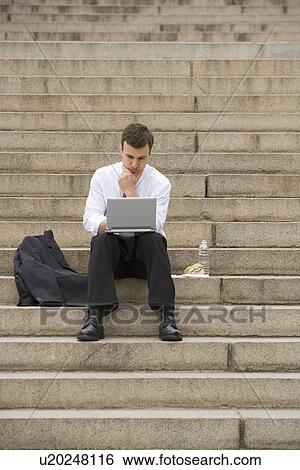 Stock Photograph - Man sitting outdoors on stairs with laptop. Fotosearch