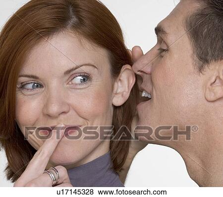 Stock Photo - Man whispering secret in woman's ear. Fotosearch