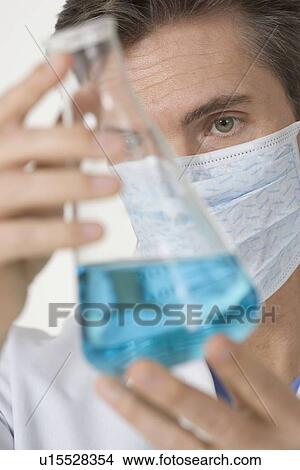 Picture - Masked scientist examining blue liquid. Fotosearch