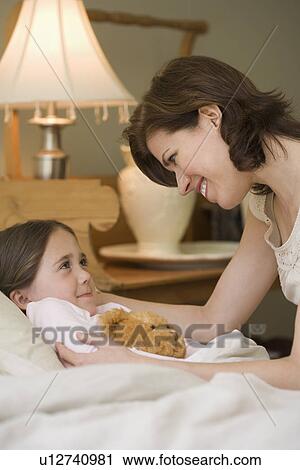 Mother tucking young daughter into bed View Large Photo Image Stock Image - Mother tucking young daughter into bed. Fotosearch