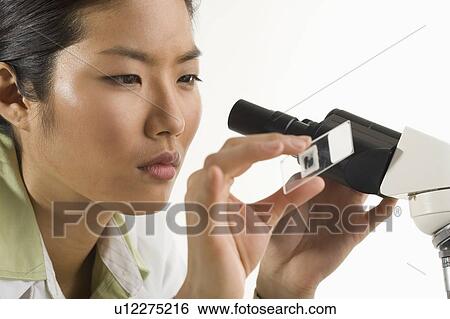 Stock Photograph - Scientist at microscope looking at slide. Fotosearch