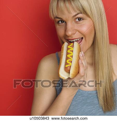 Stock Image - Studio shot of woman eating hot dog with mustard. Fotosearch