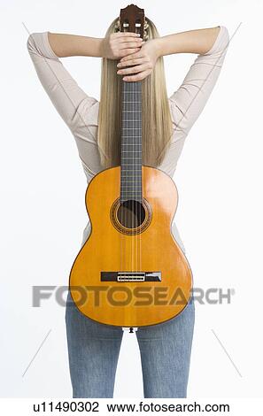 Stock Image - Studio shot of woman holding guitar against her back. Fotosearch