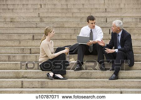 Three business people talking outdoors on stairs with laptop View Large Photo Image Stock Image - Three business people talking outdoors on stairs with laptop. Fotosearch