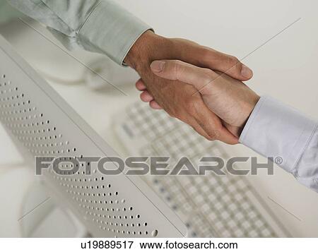 Stock Photo - Two men shaking hands over computer. Fotosearch