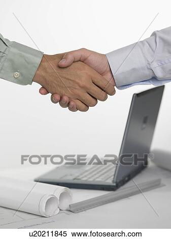 Two men shaking hands over laptop computer View Large Photo Image Stock Photography - Two men shaking hands over laptop computer. Fotosearch