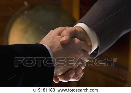 Stock Image - Two men shaking hands with globe in background. Fotosearch