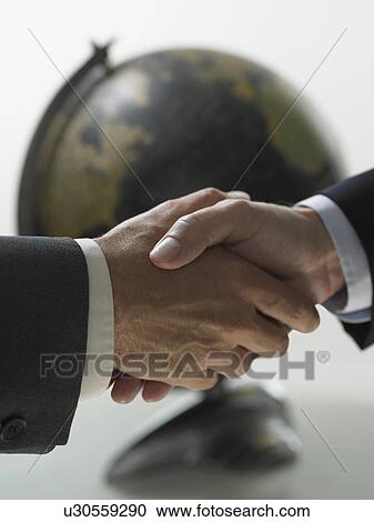 Stock Image - Two men shaking hands with globe in background. Fotosearch