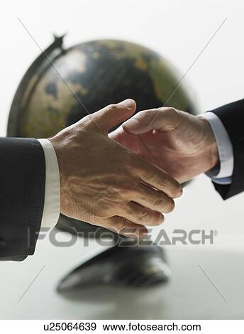 Two men shaking hands with globe in background View Large Photo Image Stock Photo - Two men shaking hands with globe in background. Fotosearch