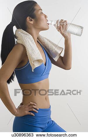 Stock Image - Woman drinking bottled water after workout. Fotosearch