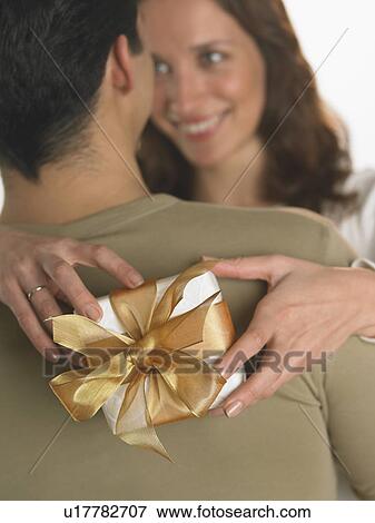 Stock Photo - Woman holding gift with arms around man. Fotosearch