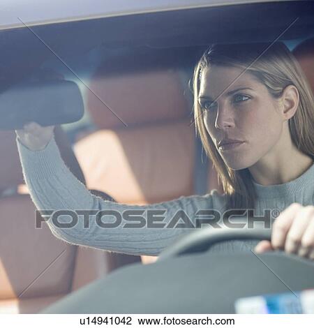 Stock Image - Woman in car adjusting rearview mirror. Fotosearch
