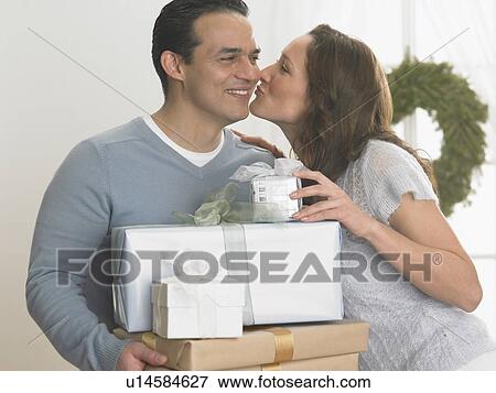 Woman kissing man holding Christmas gifts View Large Photo Image Stock Photo - Woman kissing man holding Christmas gifts. Fotosearch