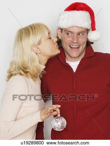 Stock Image - Woman kissing man in Santa hat. Fotosearch