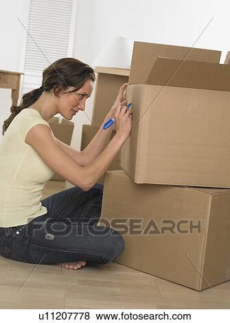 Stock Photo - Woman marking boxes on moving day. Fotosearch