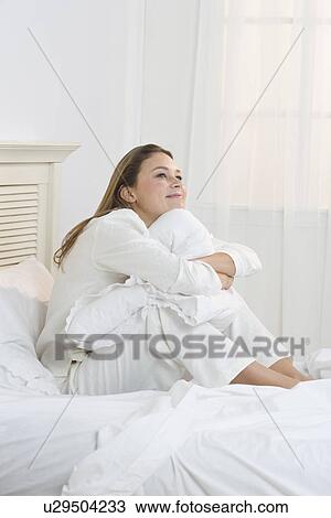 Stock Image - Woman on bed hugging her knees. Fotosearch