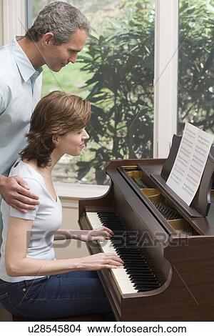 Picture - Woman playing piano with man watching. Fotosearch