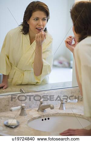 Stock Image - Woman putting on lipstick in bathroom. Fotosearch