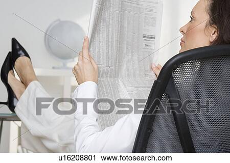 Stock Image - Woman reading newspaper business page. Fotosearch