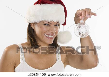 Stock Photo - Woman wearing Santa hat holding ornament. Fotosearch