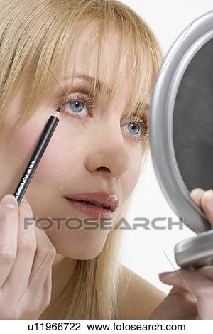 Stock Image - Woman with mirror and eyeliner. Fotosearch