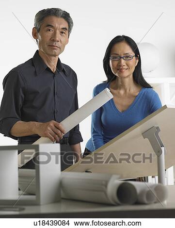 Picture - Asian businessman and businesswoman at drafting table with blueprints. Fotosearch