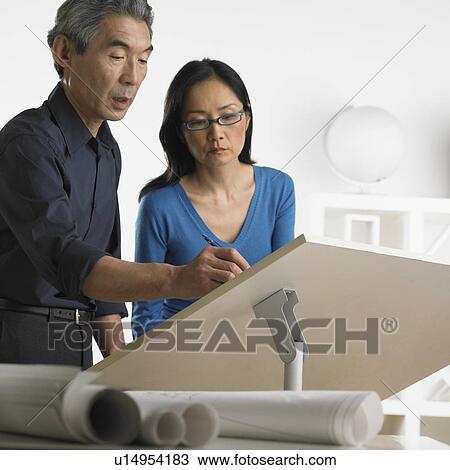 Stock Image - Asian businessman and businesswoman at drafting table with blueprints. Fotosearch