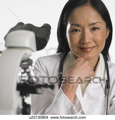 Asian female doctor smiling next to microscope View Large Photo Image Picture - Asian female doctor smiling next to microscope. Fotosearch