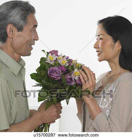 Stock Photo - Asian man giving Asian woman bouquet of flowers. Fotosearch