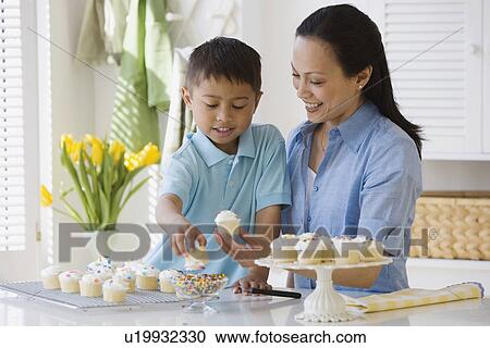 Stock Image - Asian mother and son decorating cupcakes. Fotosearch
